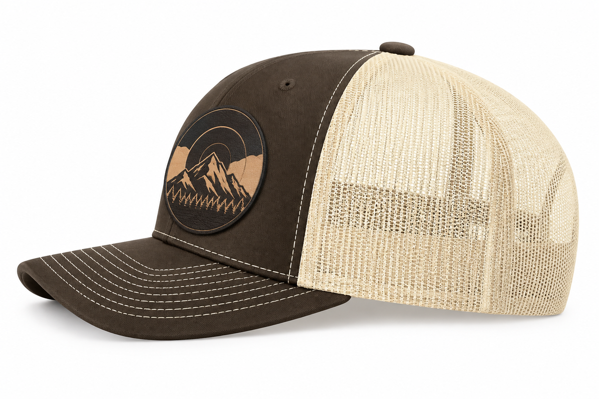 Side view of a two-tone Mountain Heritage trucker hat with a leather mountain patch and mesh back