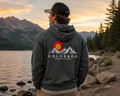 Man wearing a Colorado ClassicMountain Hoodie in heather deep gray at a Colorado mountain lake at sunset showing the back graphic