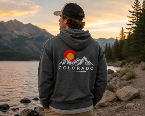 Man wearing a Colorado ClassicMountain Hoodie in heather deep gray at a Colorado mountain lake at sunset showing the back graphic
