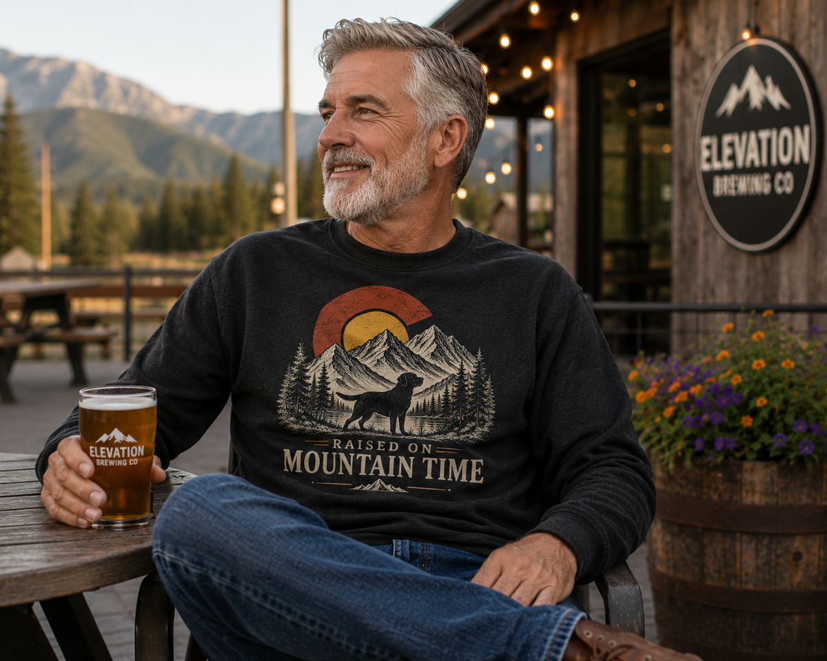 Man wearing Raised on Mountain Time sweatshirt at a Colorado mountain brewery patio at golden hour