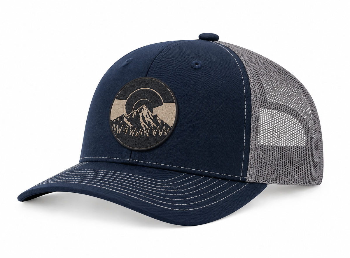 A navy blue trucker cap with a gray mesh back and a circular embroidered mountain patch on the front, shown on a white background.
