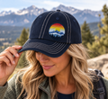 Woman wearing a navy Retro Mountain Sunset dad's cap with an offset mountain patch against a Colorado mountain backdrop