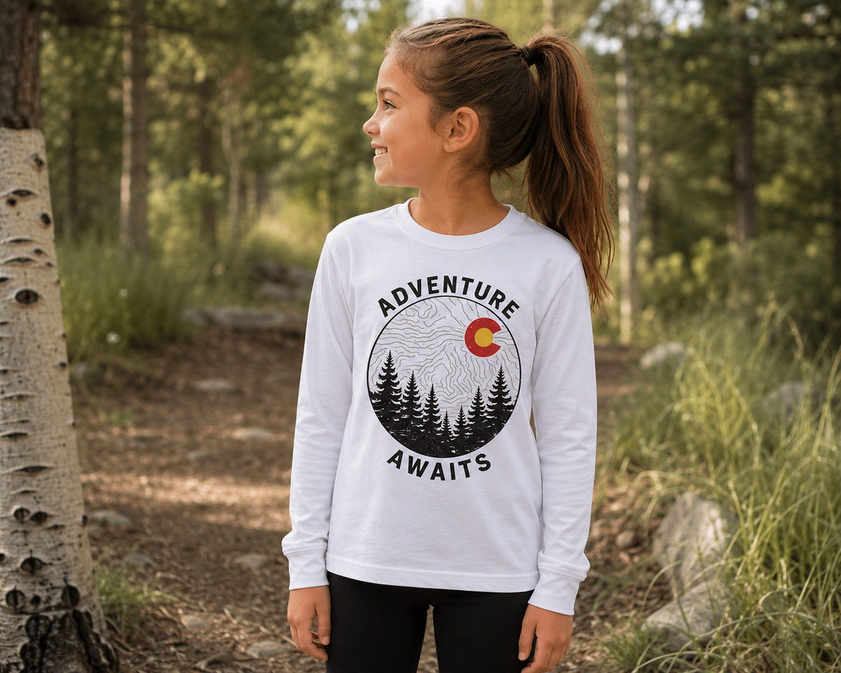 Girl wearing Youth Adventure Awaits Colorado Long Sleeve Tee in white among aspen trees showing front graphic